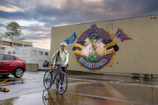 Student with bike in front of 'Kotahitanga' mural by Mr G