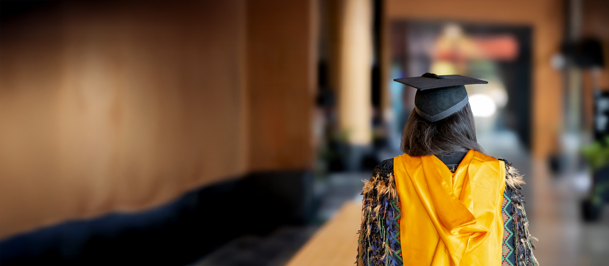 Student wearing graduation regalia walking through the Pā