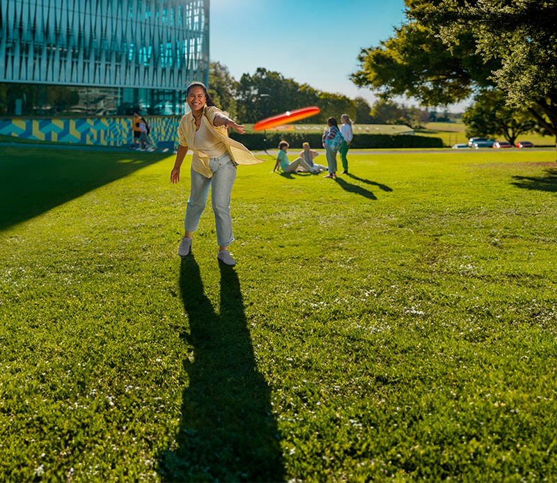 Student throwing frisbee in front of the library
