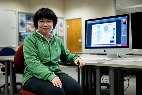 Yingyu sitting next to a computer with his design on the screen.