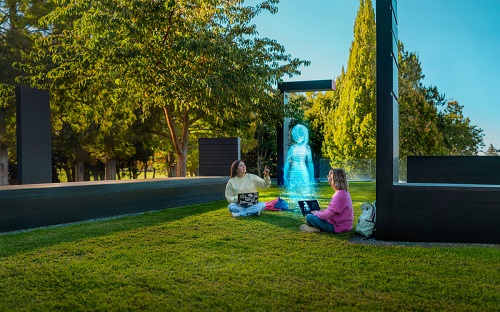Two girils sitting on grass with laptops inbetween a hologram.