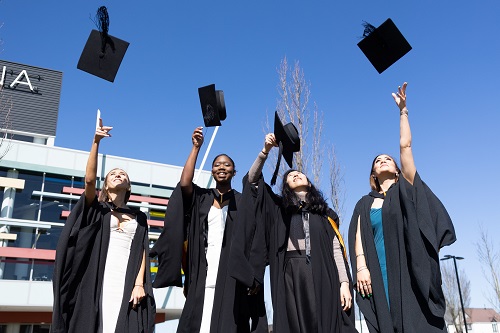 Four graduates throwing their academic hats in the sky
