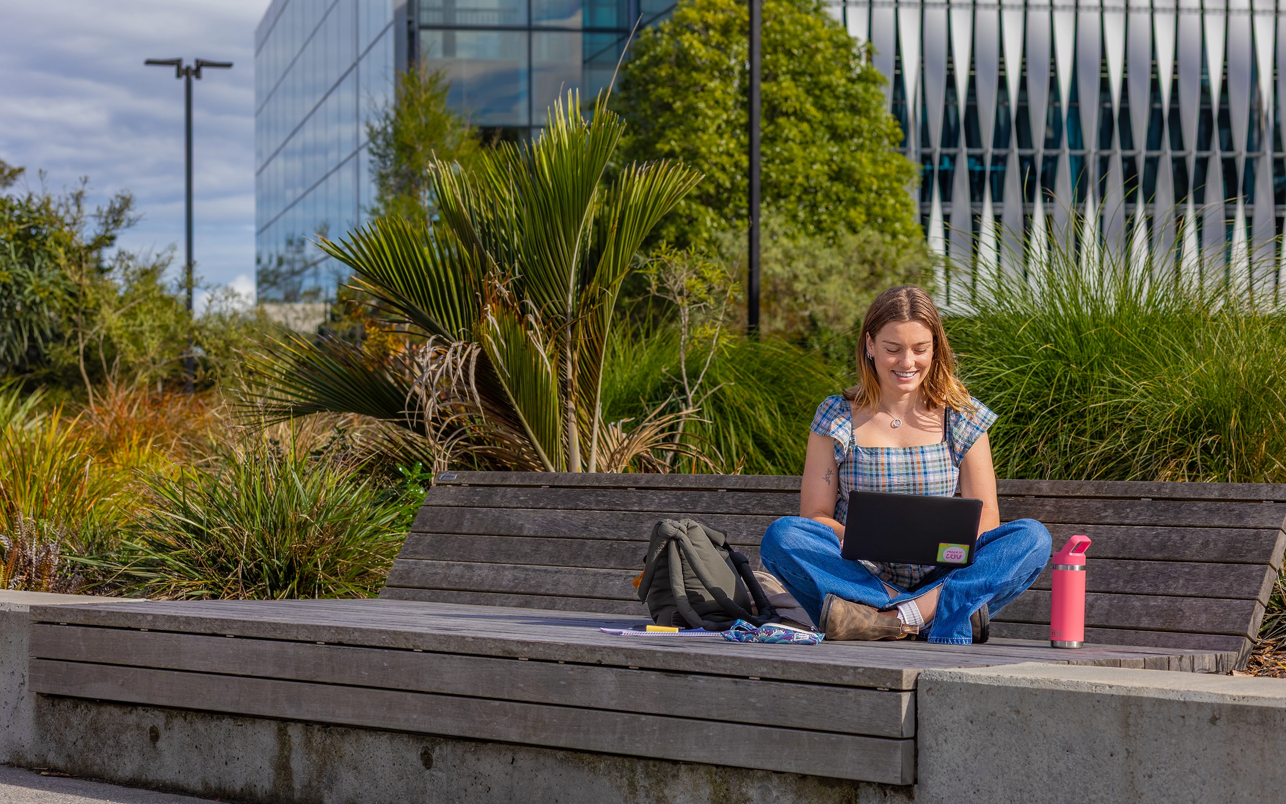  Student sitting outside the library on a bench studying, surrounded by greenery