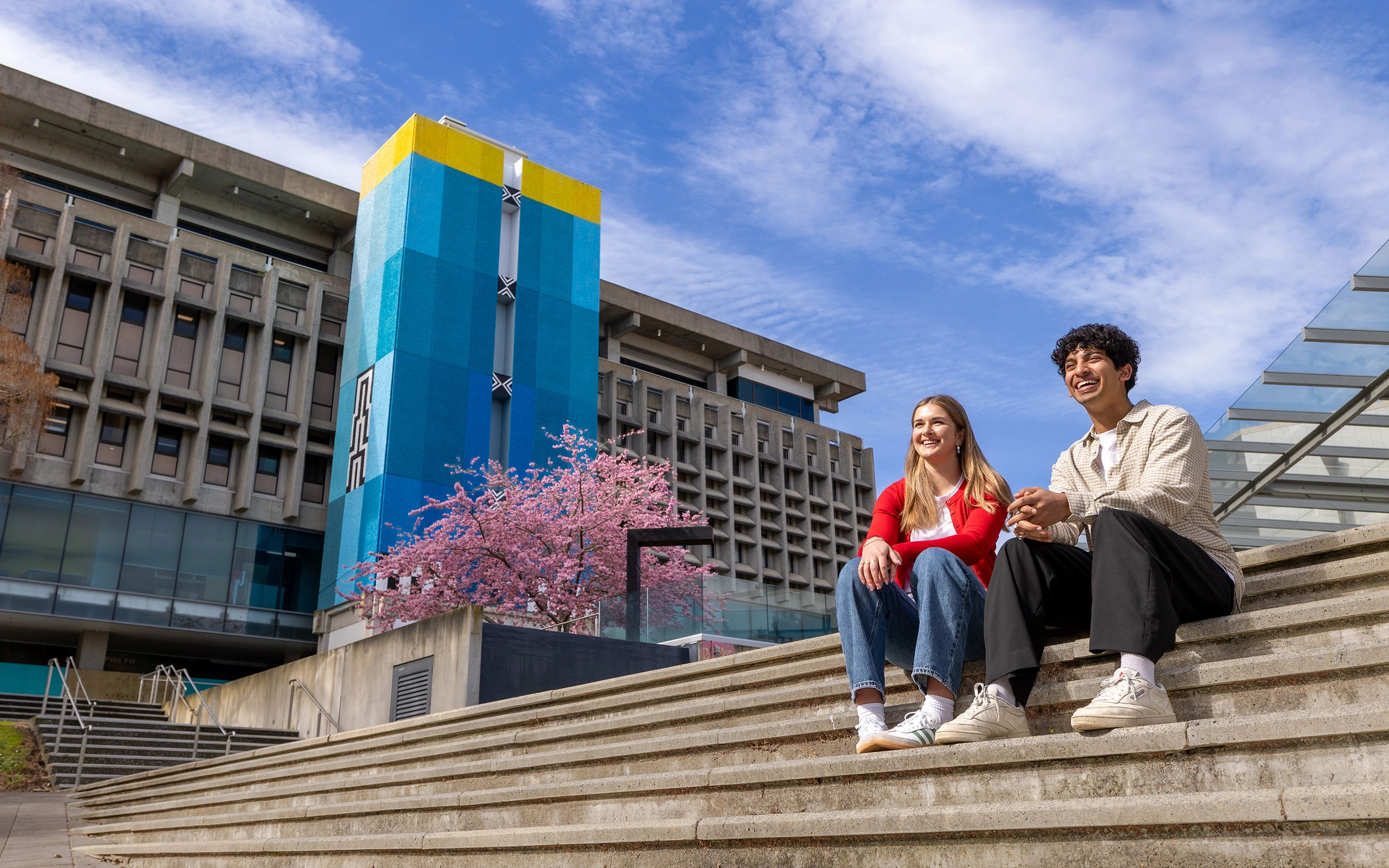 Students sitting on the steps outside the Student Centre infront of blue and yellow mural