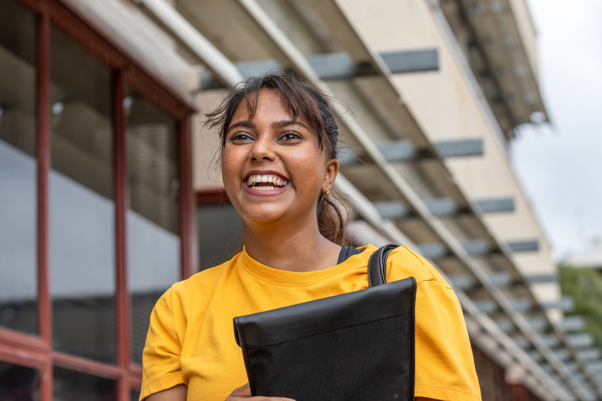 Student in yellow top smiling holding laptop